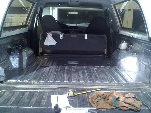 1994 Ford Bronco - Rear cargo area of a full-size SUV with the tailgate down and carpet stripped out, showing the bare ribbed sheet-metal floor and rear wheel…