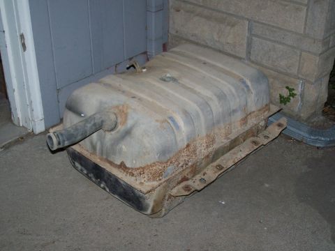 1989 Ford Bronco - A rusty fuel tank with a filler neck is shown resting on the ground next to a building.