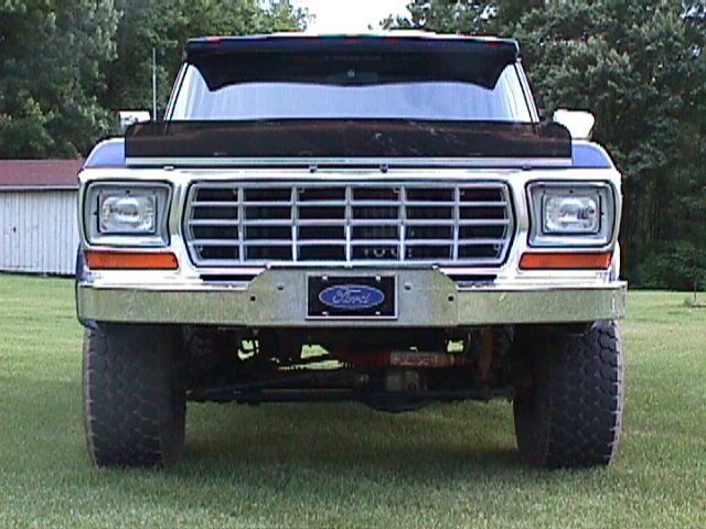 Head-on view of a lifted dark blue Ford 4x4 with chrome grille and Ford oval plate on a lawn