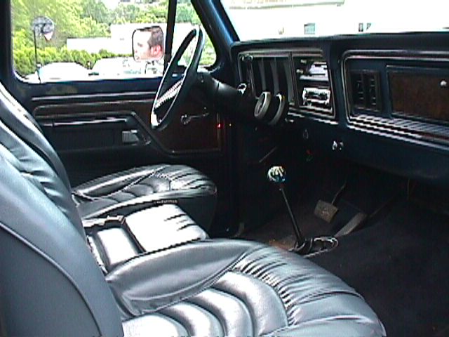 Black vinyl bucket-seat interior of 1970s Ford truck with woodgrain dash and floor shifter