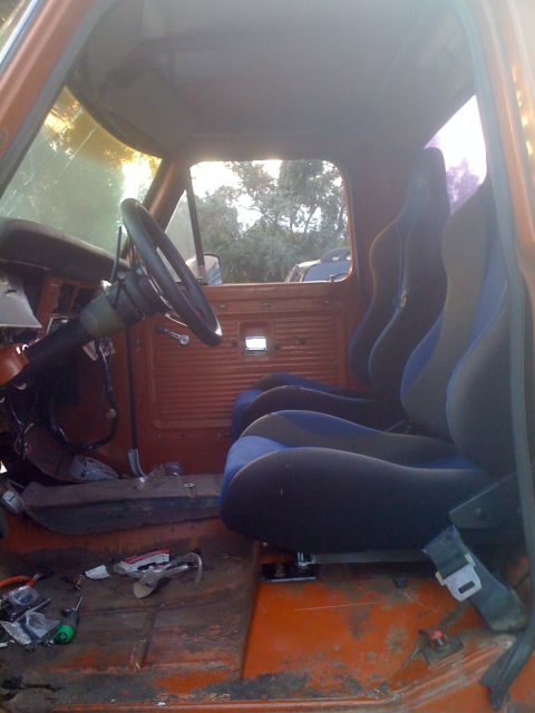 1969 Ford F-250 - The interior of a truck shows aftermarket racing seats and a cluttered floor with tools and parts.