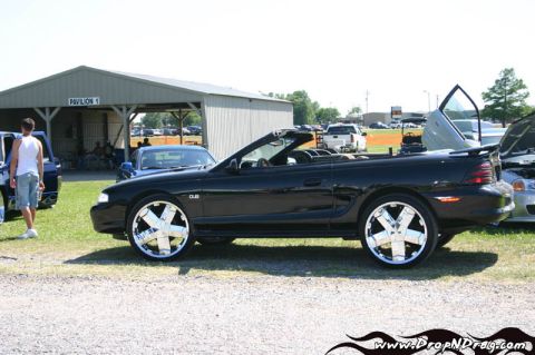 2007 Ford Mustang - Side profile of a black SN95 Ford Mustang convertible with the top down, sitting on oversized chrome DUB-style spinner wheels with low-prof…