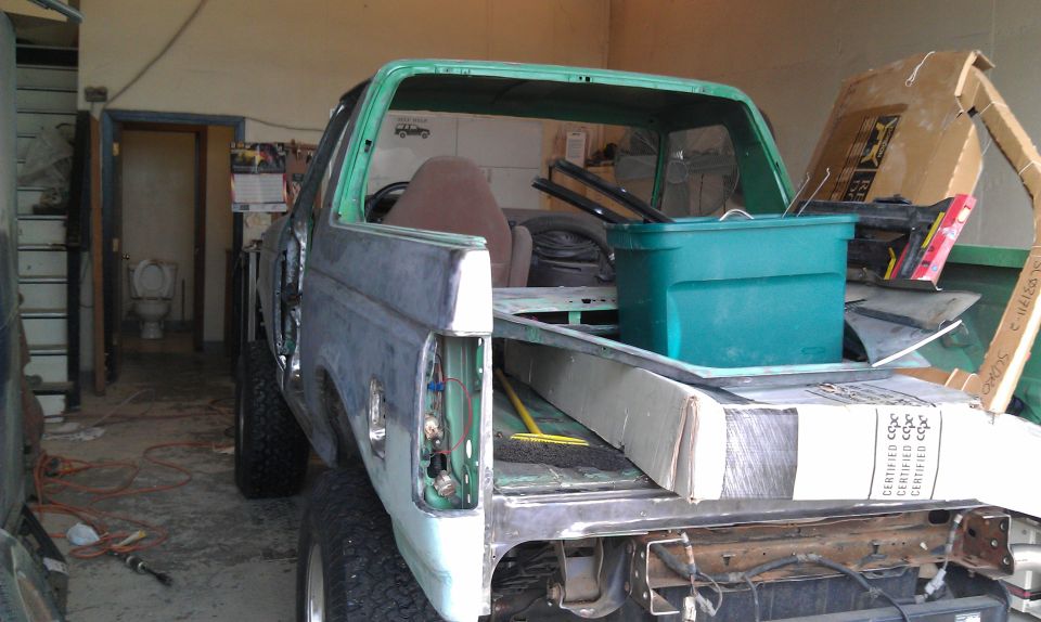 Rear view of a green Ford Bronco in a garage, bed loaded with boxes and a tote