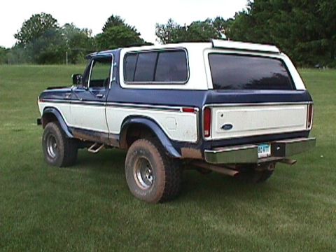 1978 Ford Bronco - This two-tone blue and white Ford Bronco is shown from the rear three-quarter angle, parked on a grassy field.