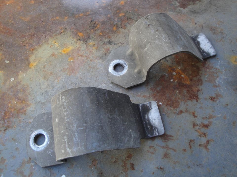 Two metal sway bar brackets on a rusty surface