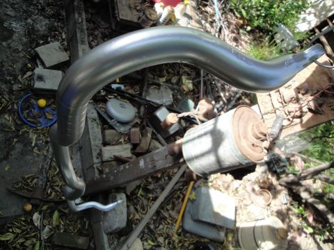 2003 Ford Taurus - A silver exhaust pipe and a rusty muffler are visible, lying amongst debris.