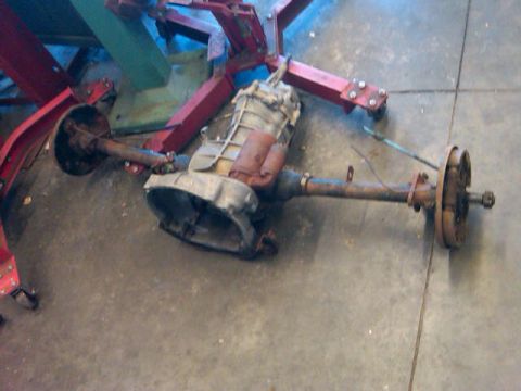 1995 Ford F-150 - A transmission and rear axle assembly are suspended from a red engine hoist in a garage setting.