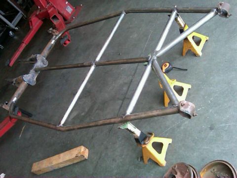 1995 Ford F-150 - A fabricated metal frame, likely for a vehicle project, is supported by yellow jack stands on a concrete floor.