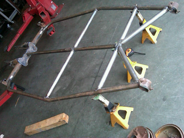 Custom roll cage frame on jack stands, with a red engine hoist in the background