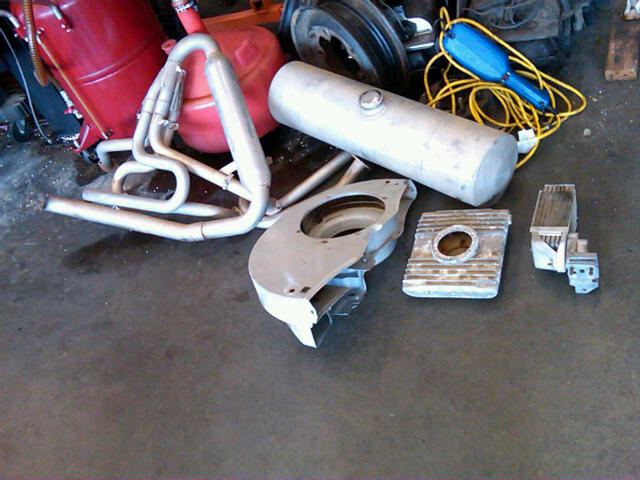 Exhaust manifold, fuel tank, and engine parts on concrete floor
