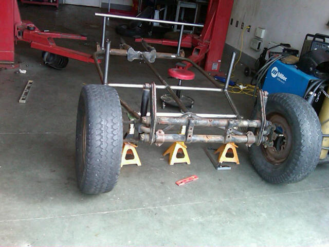 Custom buggy frame on jack stands, rear view. Miller welder visible