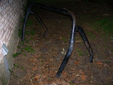 1992 Jeep YJ - A black metal roll cage is resting on the ground near a brick wall and some overgrown vegetation.