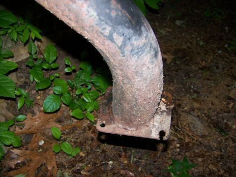 1992 Jeep YJ - A rusted exhaust pipe section with a mounting flange is shown on the ground amongst foliage.