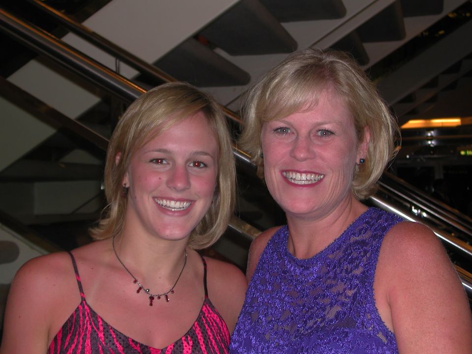 Two smiling blonde women posing indoors near a staircase