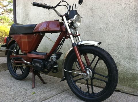 1981 Garelli Rally Sport - A brown Garelli moped is parked against a concrete wall, showing its distinctive black wheels and engine details.