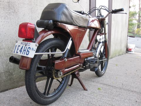 1981 Garelli Rally Sport - A brown moped is parked on a concrete surface next to a wall. The license plate reads MOPED 1E4H6.