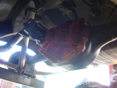 1964 Ford Fairlane - Close-up view of a vehicle's rear axle differential, showing the orange painted housing and U-joint connection.