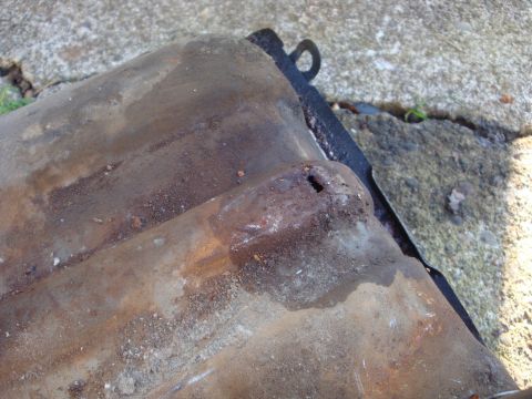 1964 Ford Fairlane - This rusted metal part has a hole and is resting on a concrete surface.