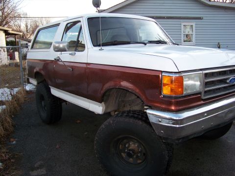 1989 Ford Bronco - Passenger-side three-quarter front view of a lifted Ford Bronco with a metallic brown lower body, white removable hardtop and white hood, p…