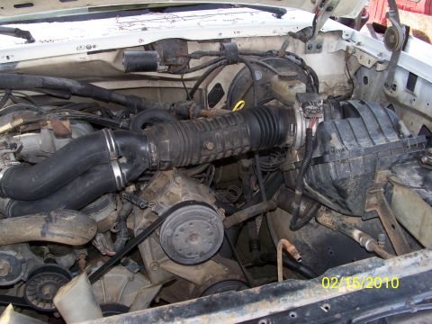 1989 Ford Bronco - Front-facing view into the engine bay of a white Ford truck with the grille, radiator and fan shroud removed, exposing the passenger-side a…