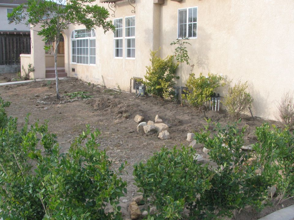 House exterior with a dirt yard, some bushes, and rocks