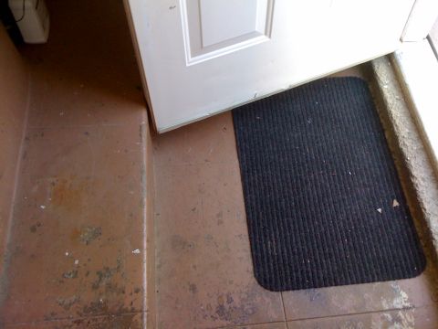 1968 Ford Mustang - A white door is ajar, revealing a black doormat on a worn, tiled entryway.