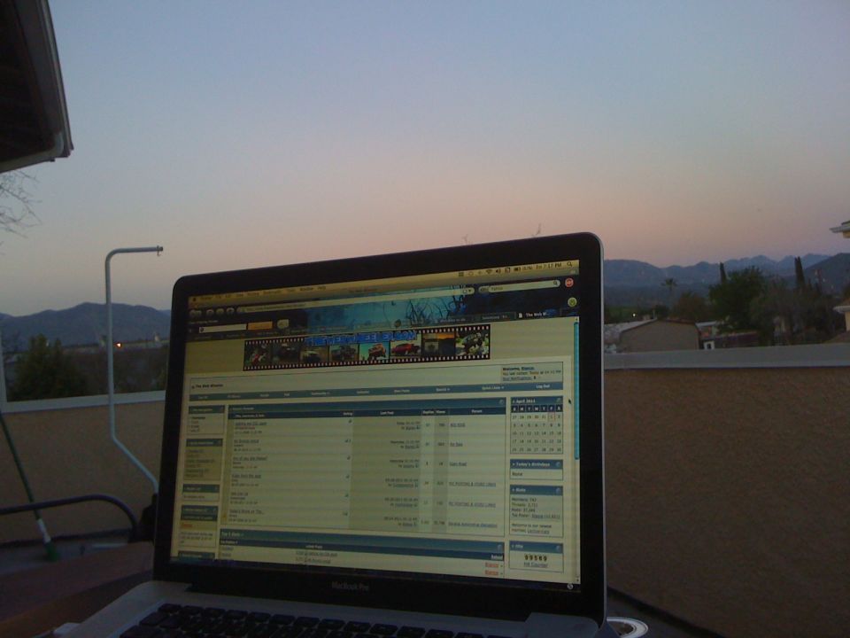 Laptop open on a patio at dusk, displaying a website with a row of car thumbnails and a table of data