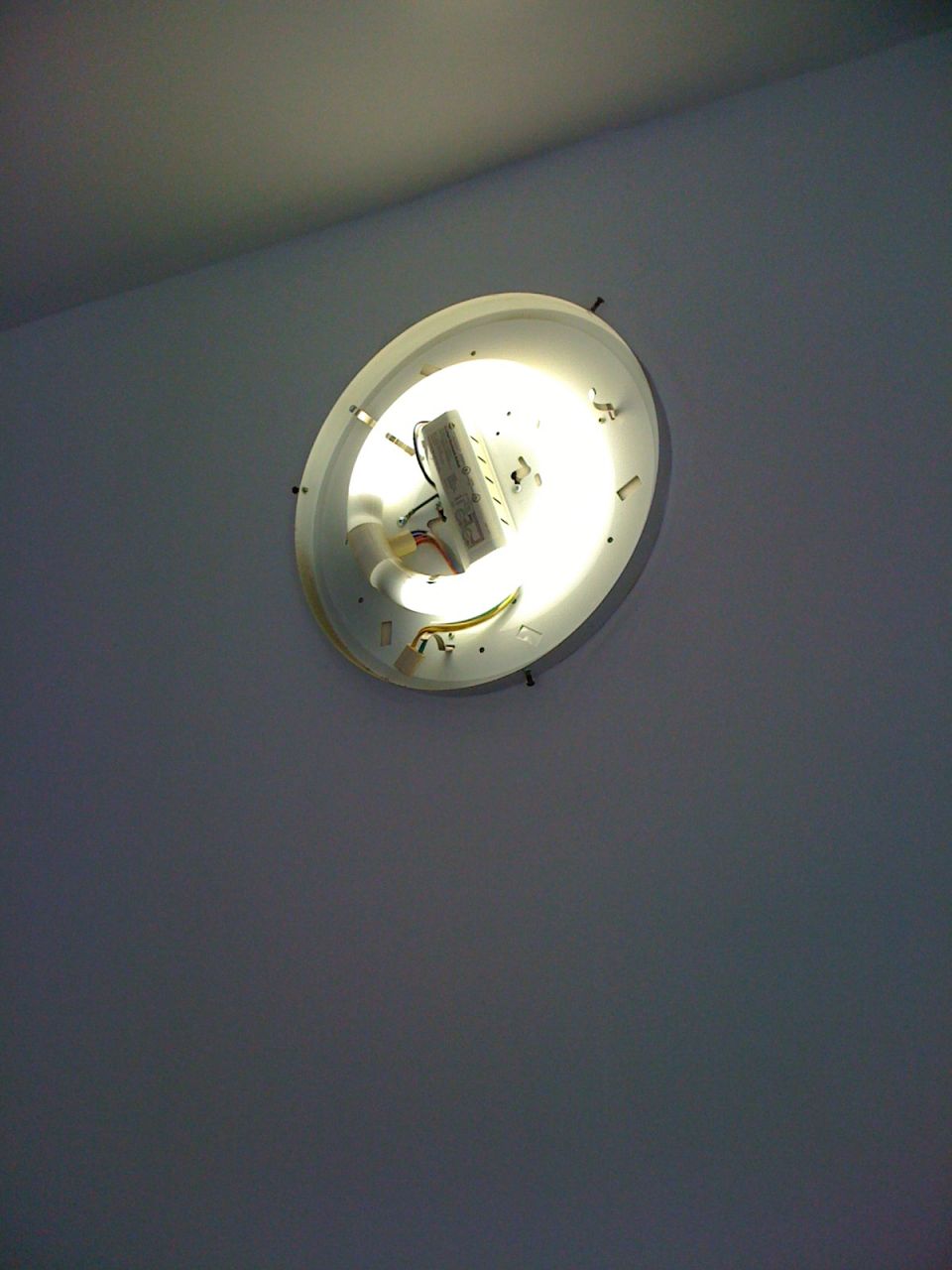 Ceiling-mounted fluorescent light fixture with exposed ballast and tube, angled view