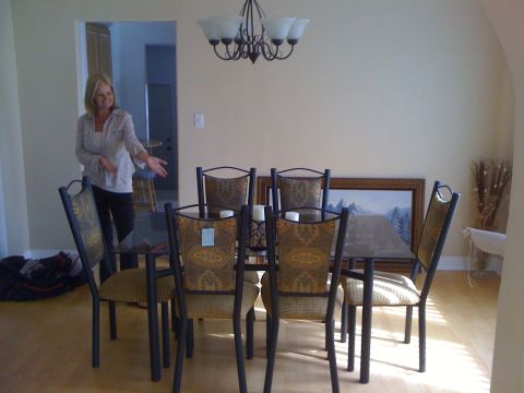 1968 Ford Mustang - A woman stands in a dining room, gesturing towards a table set with chairs and a painting on the wall.