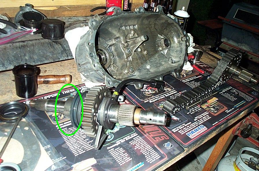 Disassembled transfer case housing and output shaft on shop mat, green circle marking a bearing area.
