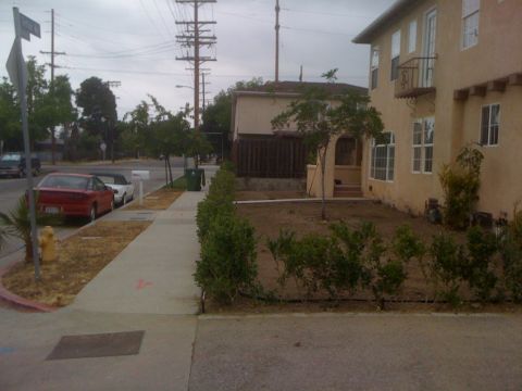 1968 Ford Mustang - A red sedan is parked on the street next to a sidewalk and a residential building.