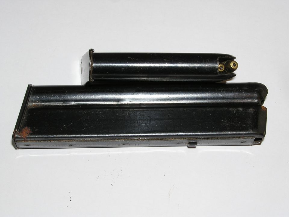 Two blued steel pistol magazines on a white background, one loaded