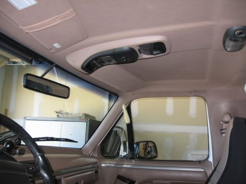 1995 Ford Bronco - Interior view of a tan-trimmed truck cab showing the headliner, overhead console, rearview mirror and exterior mirror through the windshiel…