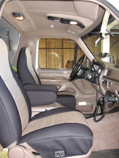 1995 Ford Bronco - Interior view of a Ford Bronco cab looking across the tan bench/bucket seats fitted with black and tan two-tone seat covers toward the stee…