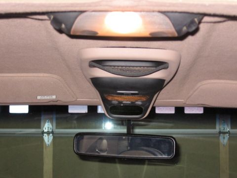 1995 Ford Bronco - Interior view of the tan headliner showing an overhead console with a dome light illuminated (orange bulb glow), map light lenses, and the…