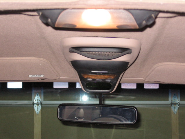 Tan overhead console with lit dome light and rearview mirror inside a vehicle