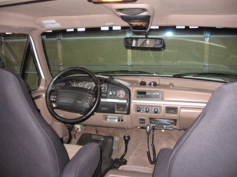 1995 Ford Bronco - Interior view from the rear seat of a 1990s Ford Bronco/truck, showing the tan dashboard, black four-spoke steering wheel, instrument clust…