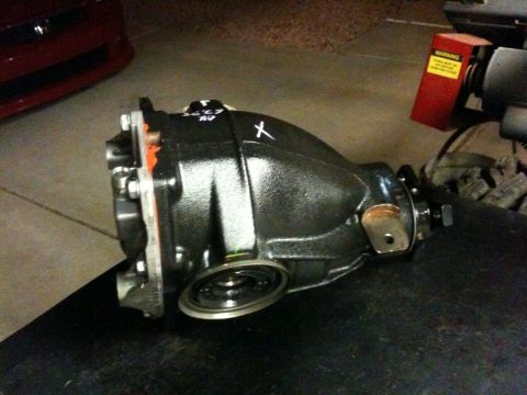2010 Dodge Challenger - A black differential housing sits on a dark surface, with a red vehicle visible in the background.
