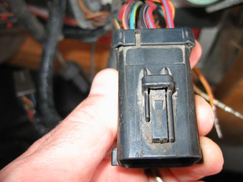 1992 Ford Bronco - A hand holds a dusty black plastic wiring harness connector with multiple colored wires visible.