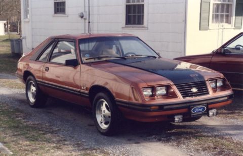 2007 Ford Mustang - A brown 1985 Ford Mustang GT is parked next to another vehicle in front of a building.