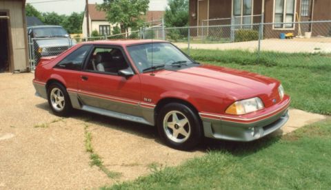 2007 Ford Mustang - This red 1987 Ford Mustang GT coupe is shown from a three-quarter front angle, parked outside a residential building.
