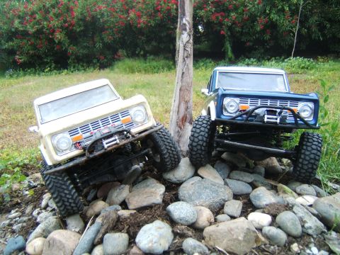 1988 Ford Bronco - Two RC rock crawlers, resembling early Ford Broncos, navigate a challenging rocky path.