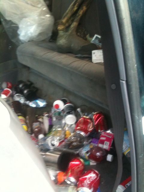1994 Ford Bronco - The interior of a vehicle is filled with trash, including numerous cans and bottles.