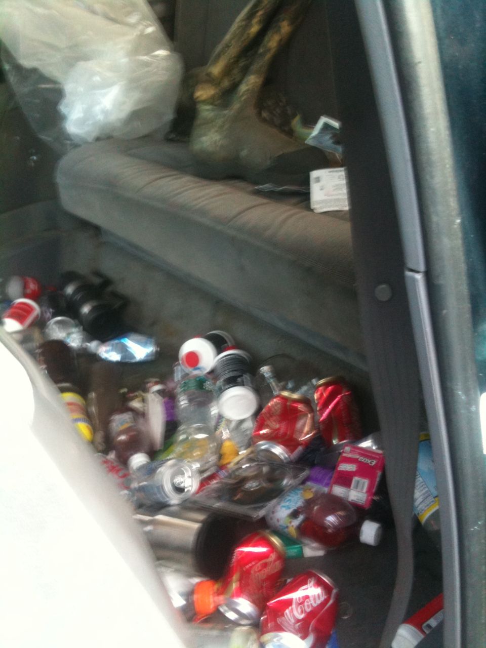 Interior of a car filled with trash, including cans and bottles. A plastic bag and some debris are on the seat