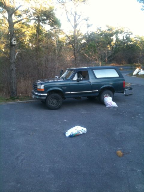 1994 Ford Bronco - A dark green 1994 Ford Bronco is parked on an asphalt surface with trees in the background.