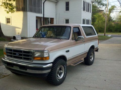 1996 Ford Bronco - A two-tone brown and white 1996 Ford Bronco is parked in front of a house.