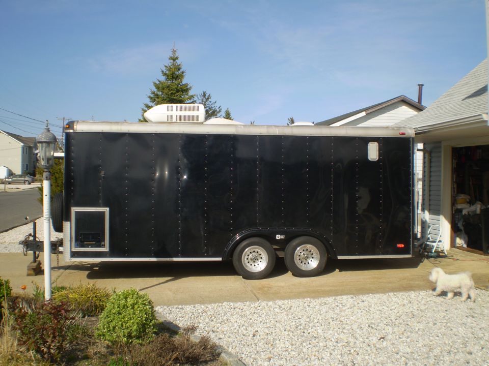 Black enclosed trailer with AC unit on roof, parked in driveway