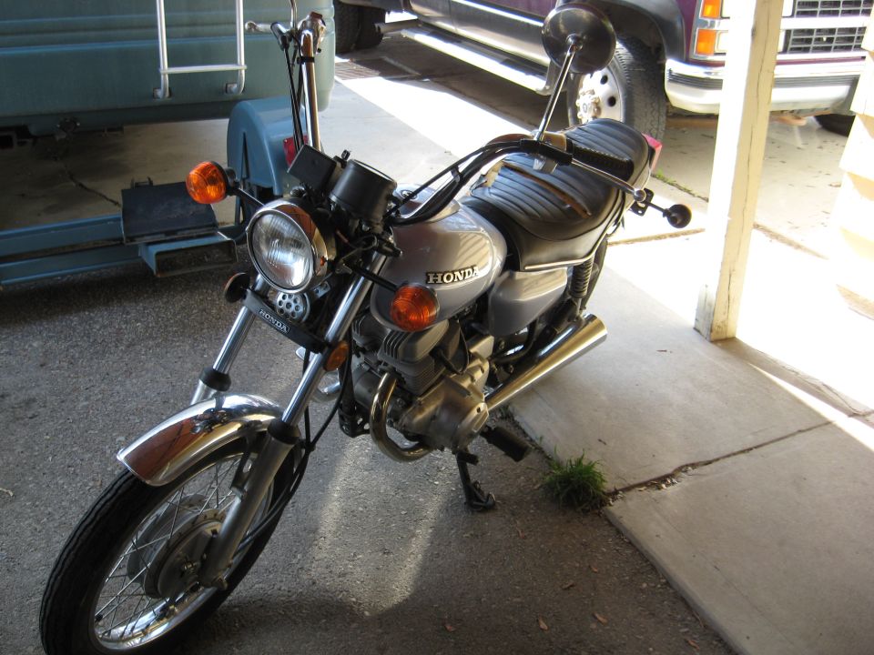 Silver Honda motorcycle parked under a carport, front-left three-quarter view.