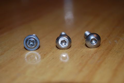 1991 Ford Festiva - Three metal screws are shown on a wooden surface, with two having hexagonal drive heads and one having a cross-head drive.