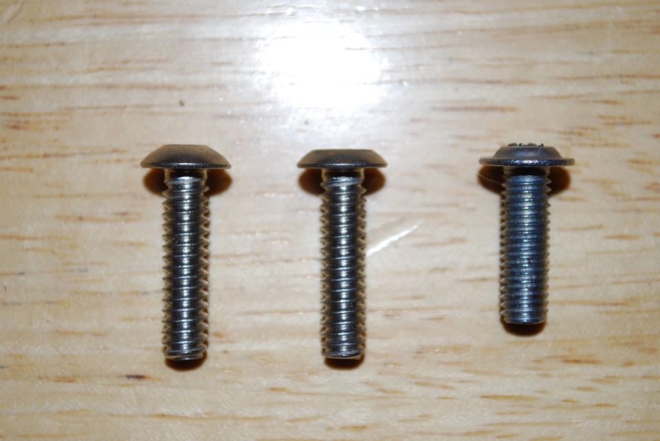 Three metal screws with threaded shafts and domed heads on a wooden surface
